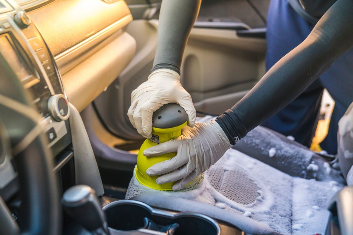 a man cleaning car interior by use foam chemical  and scrubbing machine.